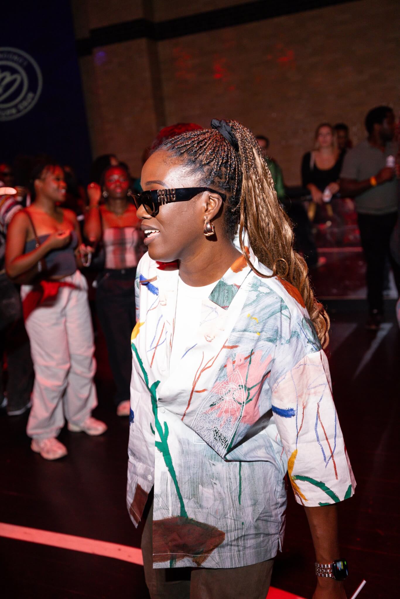 Woman wearing sunglasses and a patterned shirt dancing at an indoor African music festival demonstrating the African creative economy
