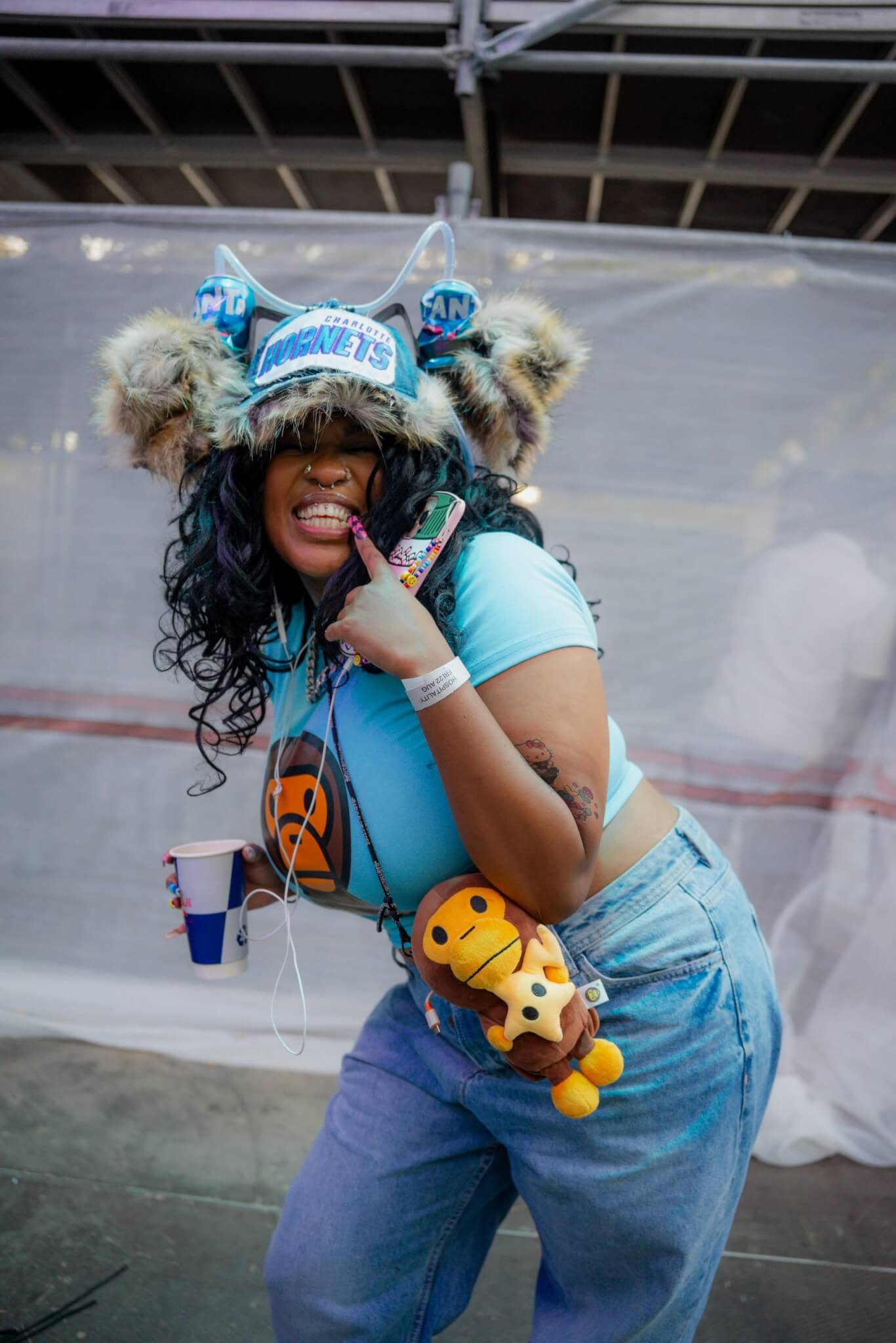 African creative economy: Woman in a blue vibrant outfit and fluffy accessories posing playfully with a drink at an outdoor event