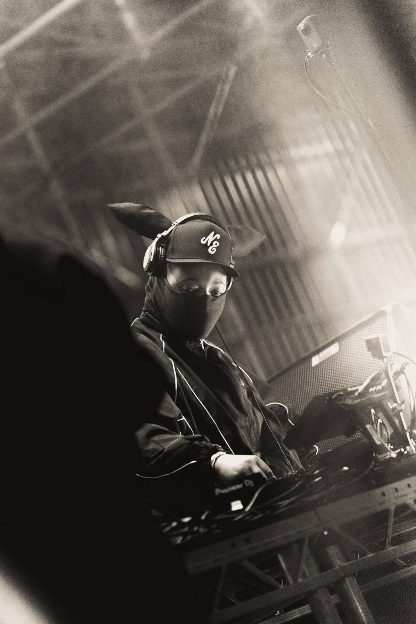 Black-and-white photo of a DJ performing on stage under bright spotlights - TMG talent
