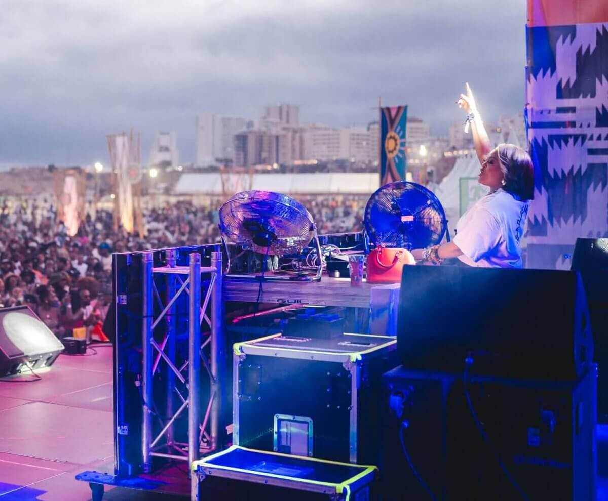 TMG talent: DJ performing on an outdoor rooftop stage overlooking a city skyline at sunset.